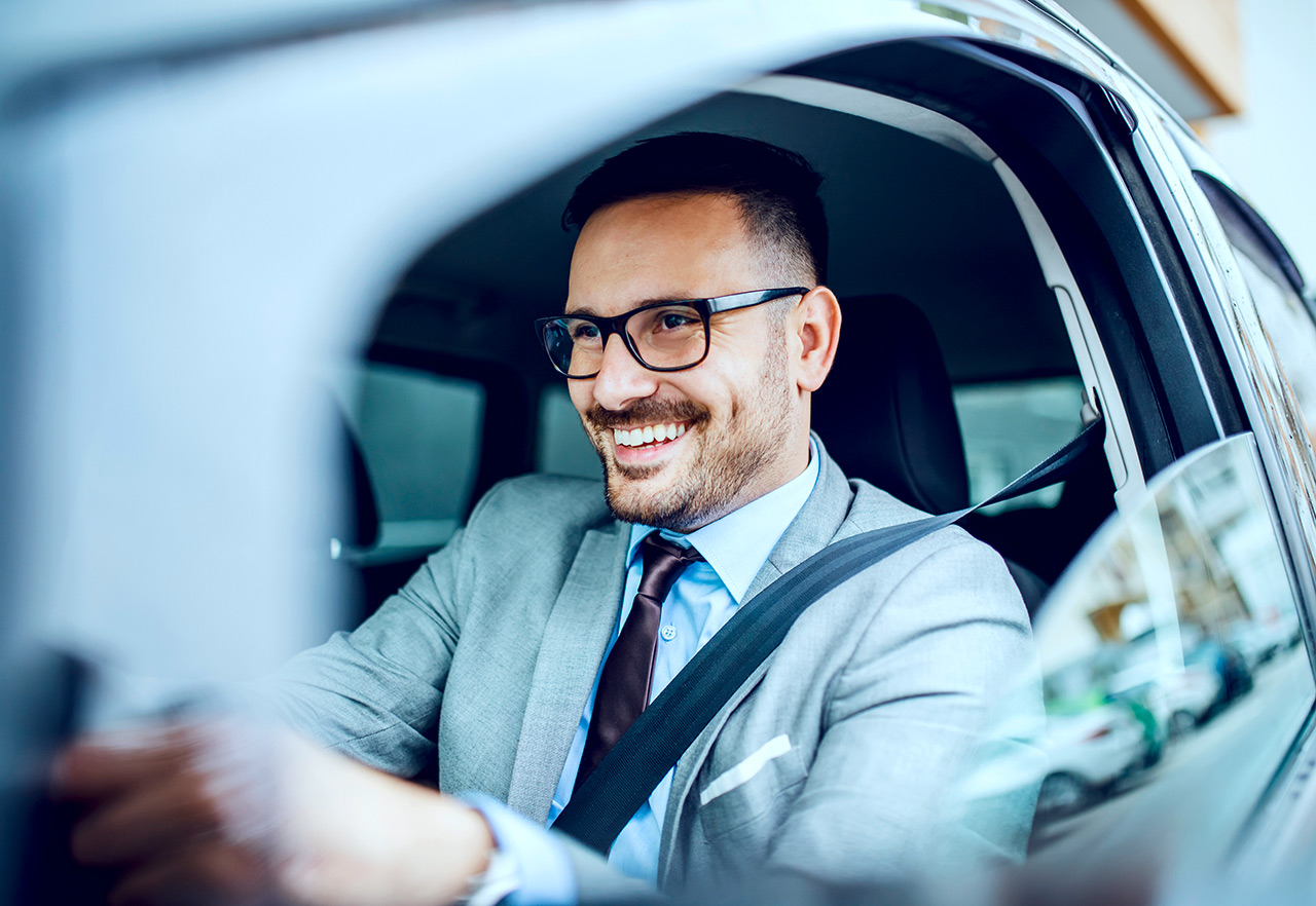 Mann im Anzug ist lachend auf dem Weg zur Arbeit mit seinem Auto.